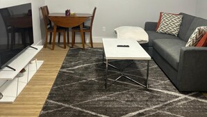 Uma sala de estar com televisão, sofá, mesa de centro e uma mesa de jantar com cadeiras.