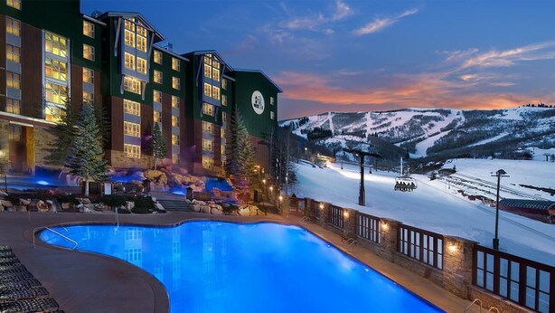 Un hôtel doté d’une grande piscine intérieure, avec une piste de ski en arrière-plan et une vue sur des montagnes enneigées.