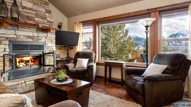 A cozy living room with a stone fireplace, comfortable seating, and large windows offering a mountain view. - Adorable Montana Cabin by Yellowstone! (Emigrant)