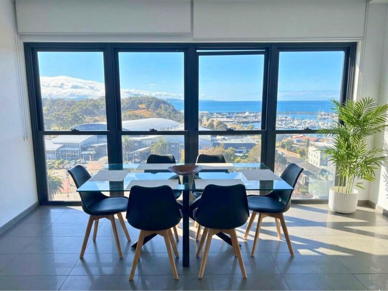 Ein Essbereich mit Tisch und Stühlen, große Fenster mit Blick auf eine Küstenlandschaft.