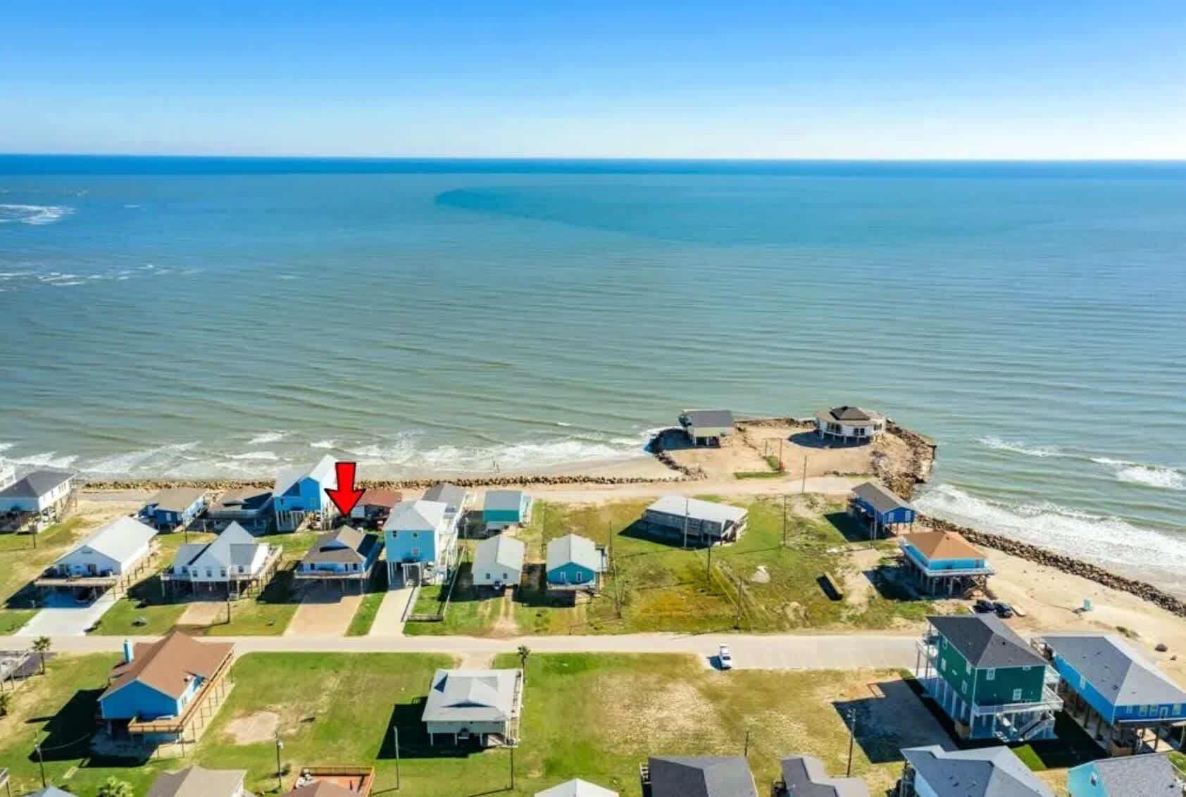 Luchtbeeld van een kustgebied met huizen, een strand en een rotsachtige landtong.