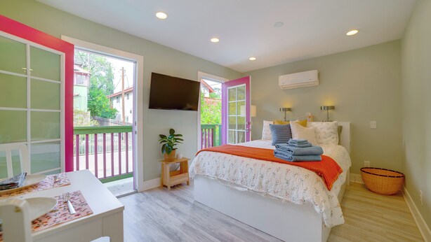 Un dormitorio con cama, una mesa, una silla, un televisor y un balcón con vistas al exterior.