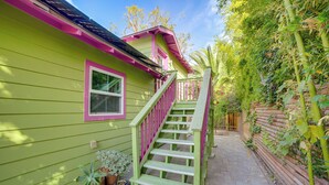 Una casa verde con un ventanal rosa y una escalera de madera que sube a un porche.