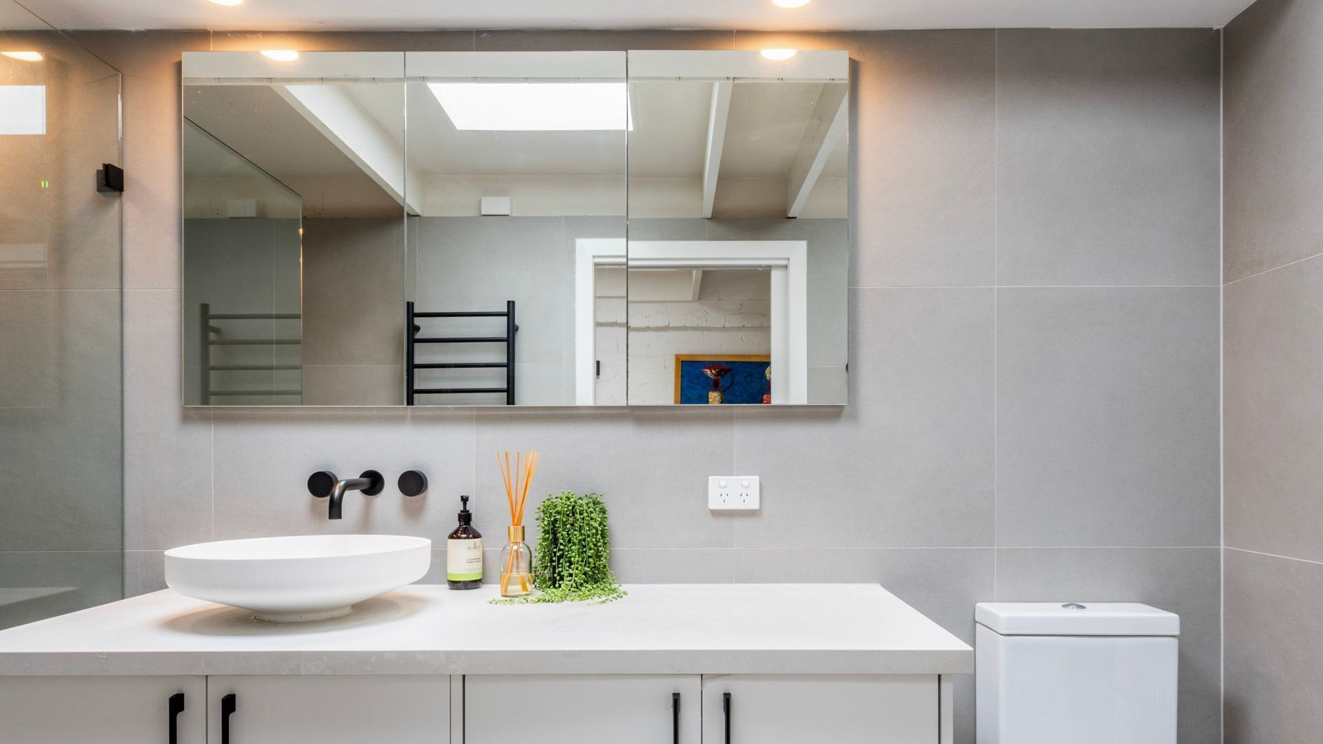 A modern bathroom with a large mirror, white sink, and cabinets.