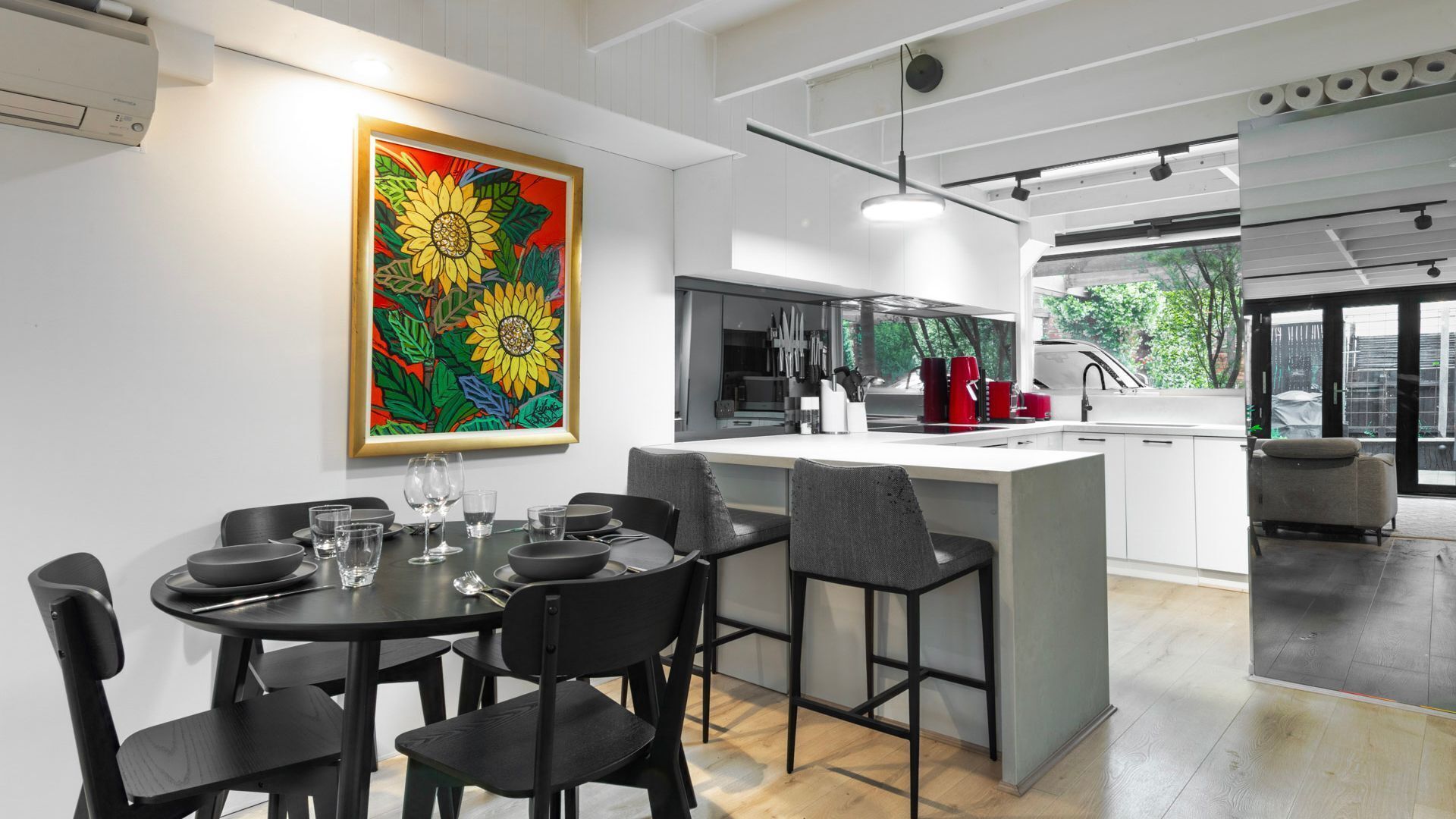 Une cuisine moderne avec un îlot central, un coin repas avec des chaises et un grand tableau représentant des tournesols accroché au mur.