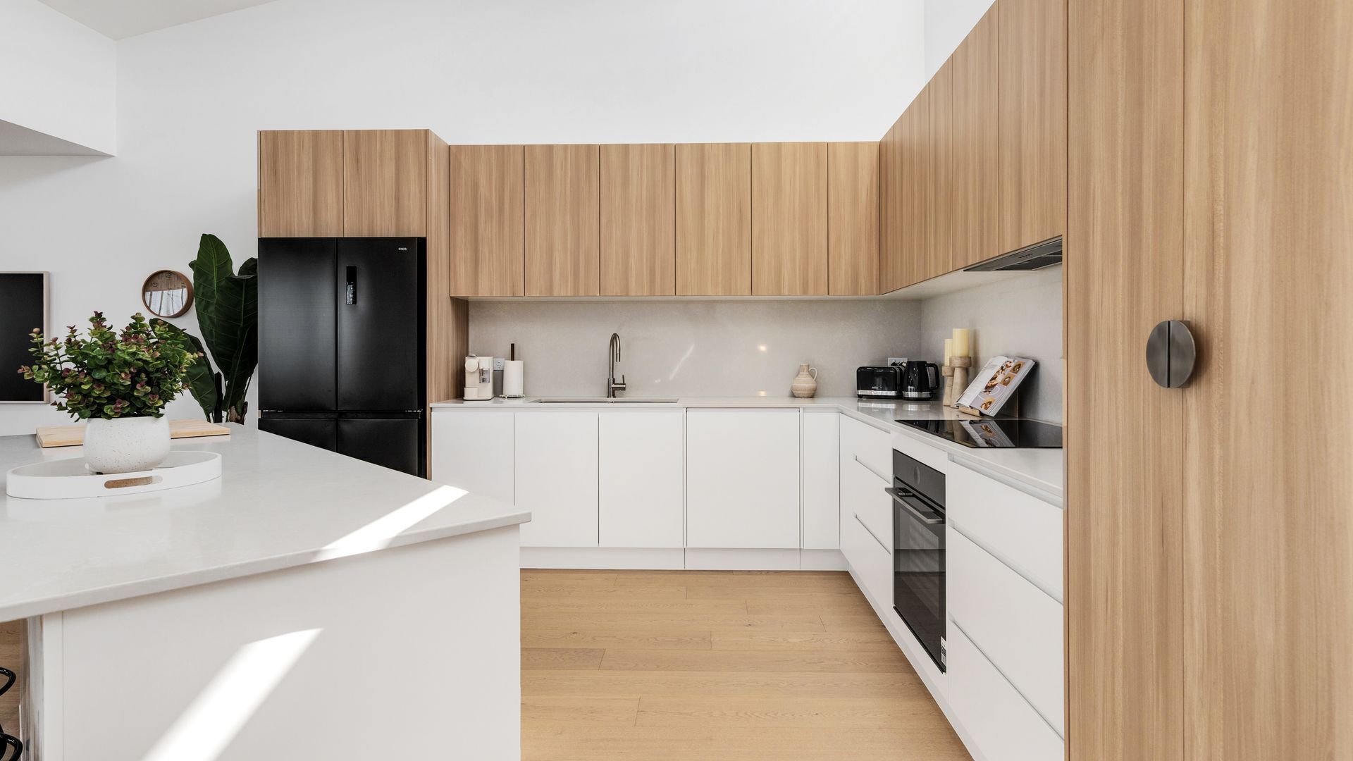 A modern kitchen with white cabinetry, a black refrigerator, and a wooden countertop.