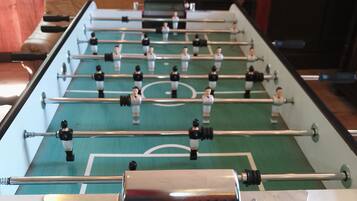 Una mesa de fútbol de mesa con superficie de juego verde y barras de metal, frente a una pared de madera.