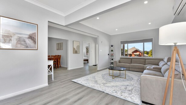 A spacious living room with a large sofa, a coffee table, and a floor-to-ceiling window offering a view of a house. - Cessnock Country Gateway to Vineyards View (Cessnock)