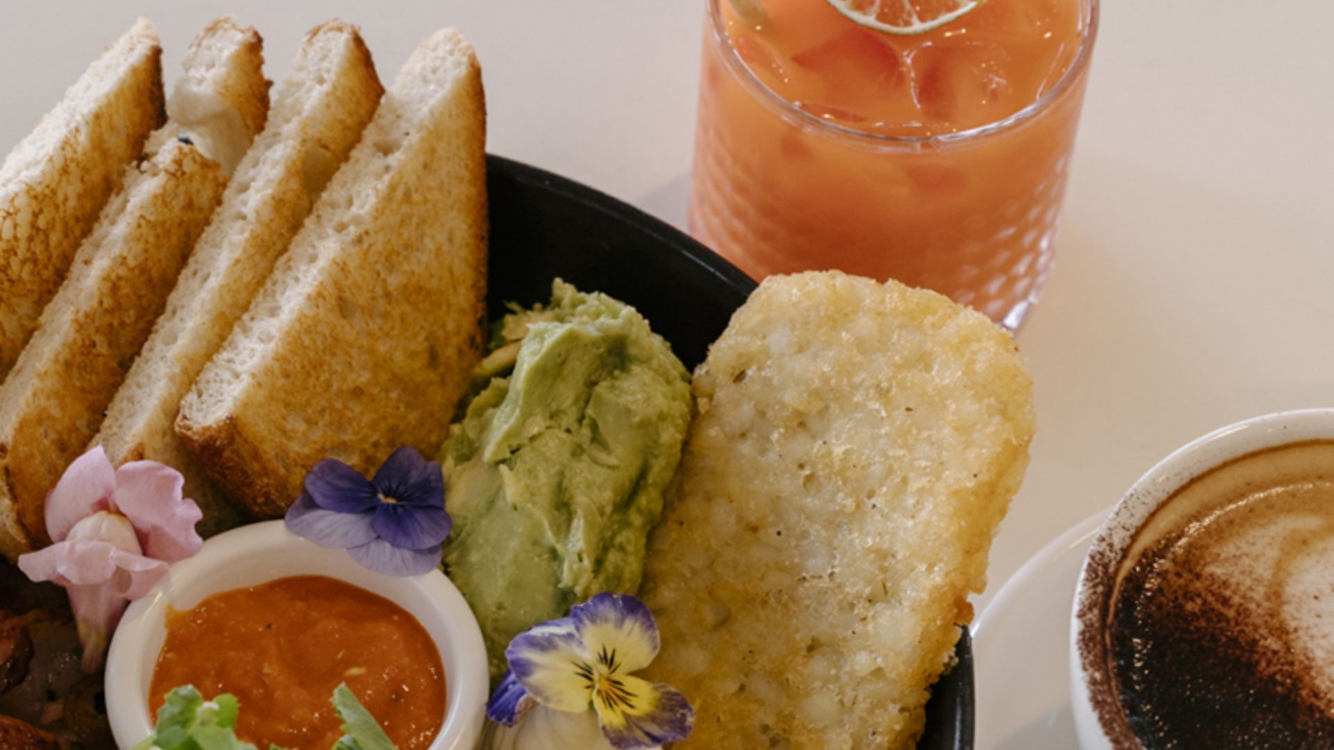 En tallerken med ristet brød, guacamole, et friturestegt element, en lille skål salsa og et glas isdrik.
