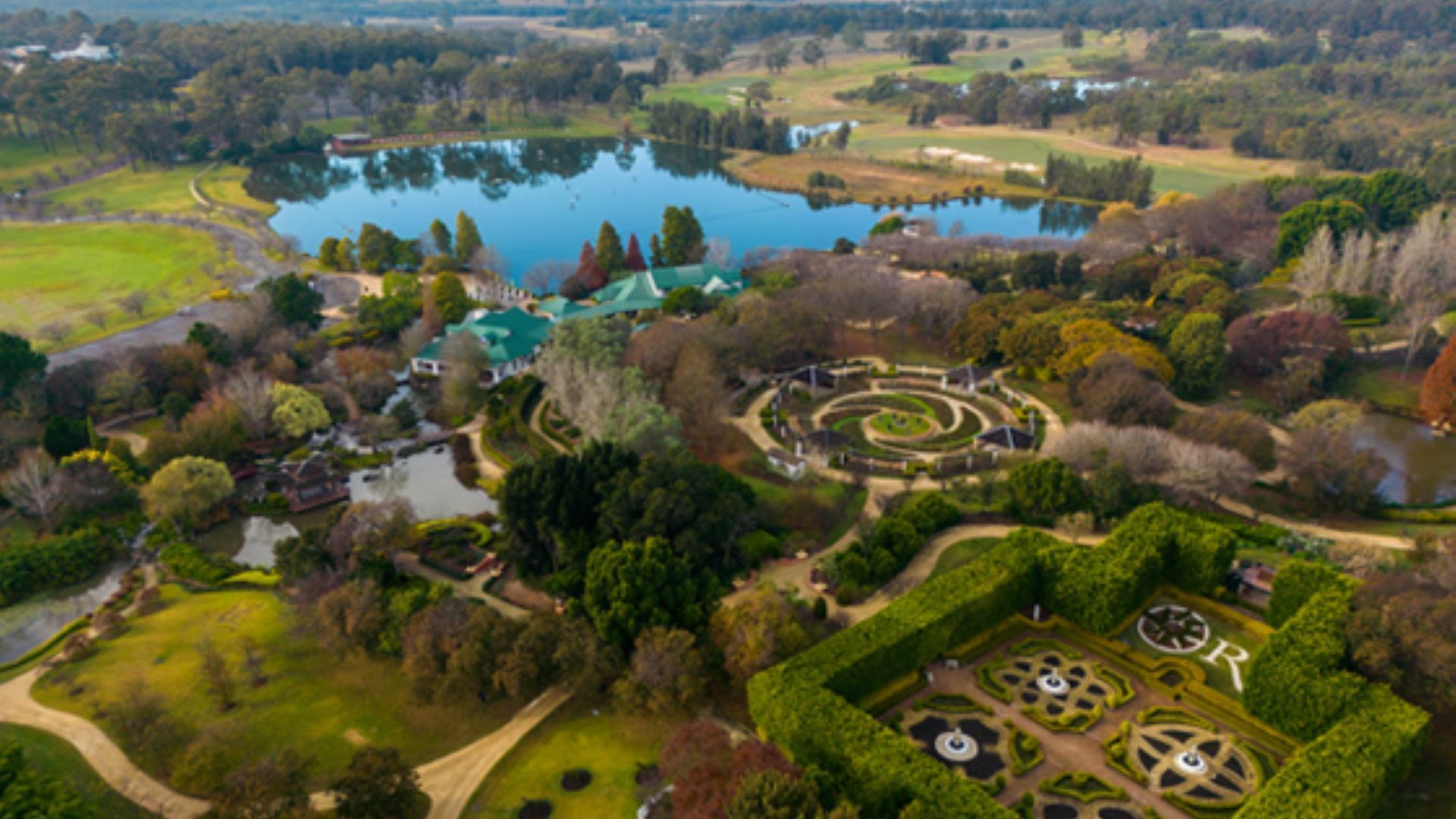 Eine Vogelperspektive eines Parks mit einem See, gepflegten Gärten und einer rundförmigen Springbrunnenanlage.