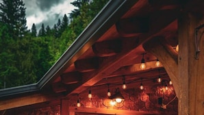 A wooden cabin with a glass door entrance, a wooden deck, and a stone wall. - Secluded Retreat | Pool,HotTub,Sauna,Firepit,Views (Meadow Creek)