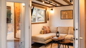 A cozy living room with a sofa, a small round table, and a window with a view of trees. - Secluded Retreat | Pool,HotTub,Sauna,Firepit,Views (Meadow Creek)