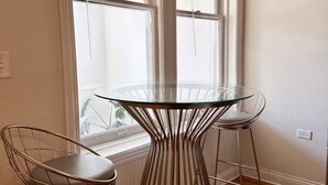 A dining area with a glass table and wireframe chairs, positioned near a window with blinds. - Flexhome Wicker Park • Stylish 2BR • Sleeps 6 (Chicago)