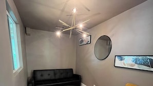 En moderne stue med en sort sofa, en gul lænestol, et rundt sofabord, en loftlampe, et rundt spejl og et indrammet billede på væggen.
