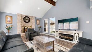 A modern living room with a fireplace, leather sofas, a coffee table, and a large TV mounted on the wall. - Houston Energy Corridor Home (Houston)