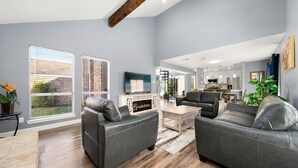 A spacious living room with grey sofas, a fireplace, and large windows. - Houston Energy Corridor Home (Houston)