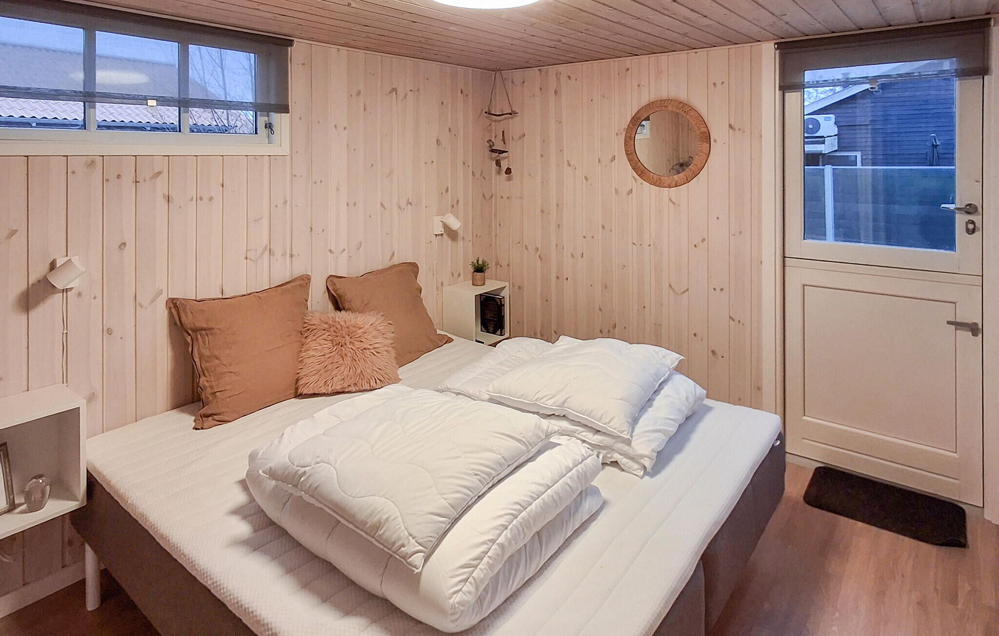A bedroom with a bed, pillows, a bedside table, a mirror, and a window.
