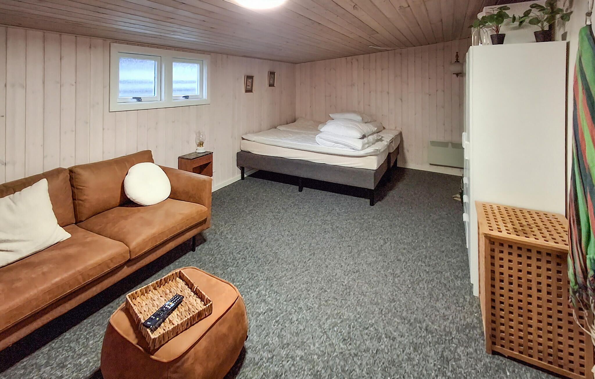 Une pièce avec un canapé marron, un lit, une petite table et un plancher en bois.