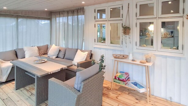 A cozy living room with a sofa set, a small table, and a wicker chair. There is a shelf with decorative items and a window with curtains. - Lovely home in Sjølund with WiFi (Sjølund)