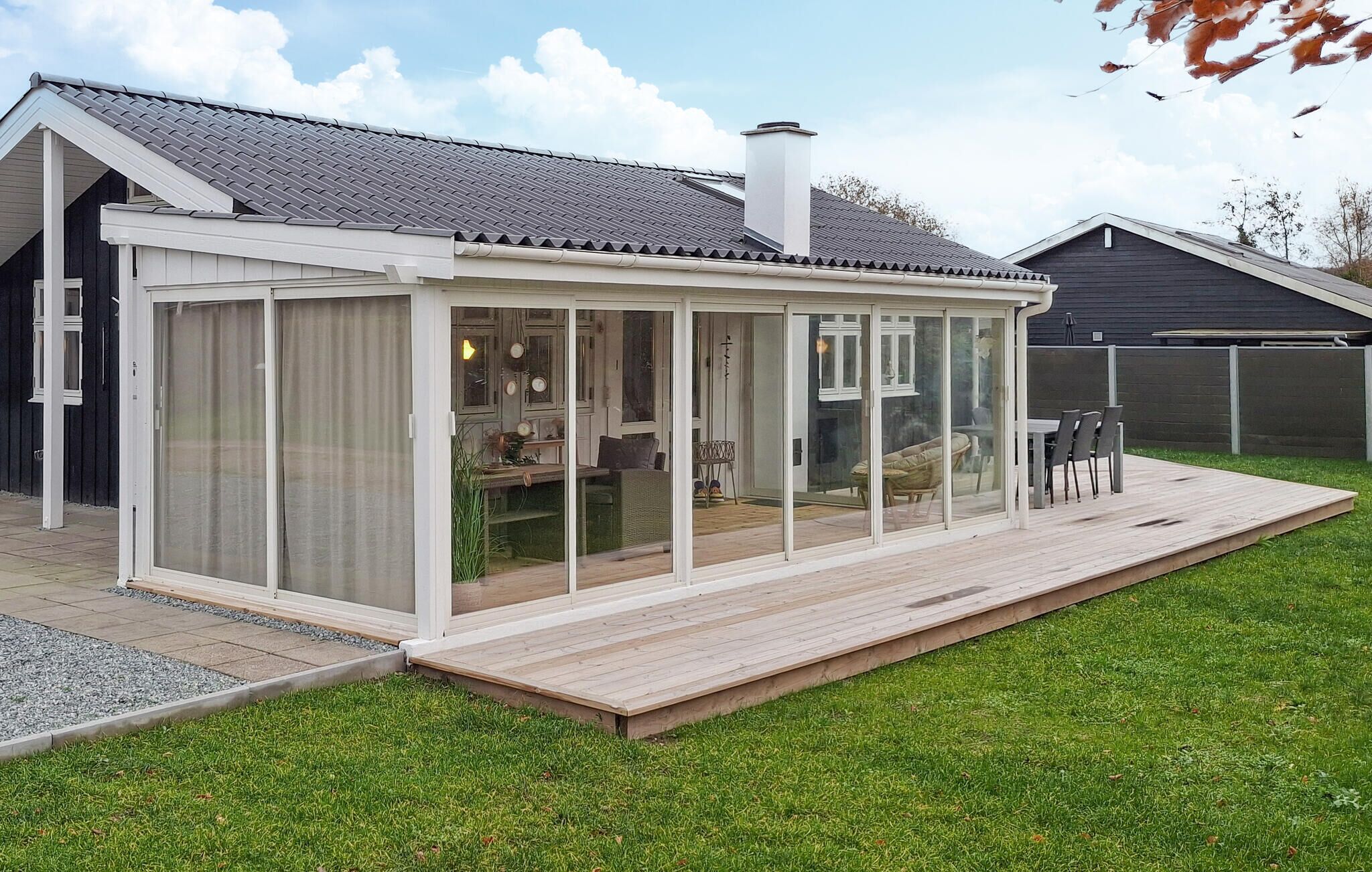 A covered patio area with a glass enclosure, a wooden deck, and a grassy yard.