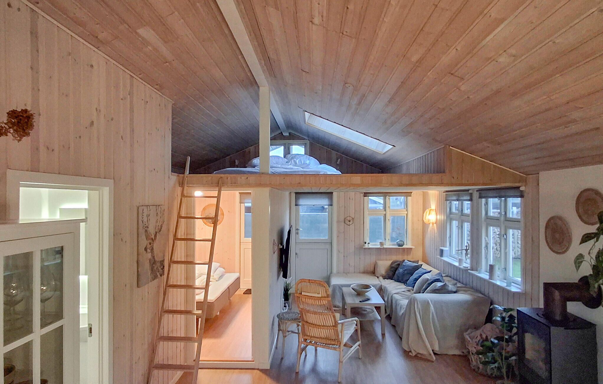 A loft-style bedroom with a skylight, a wooden staircase, a sofa, and a dining area.