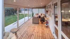 A covered outdoor area with a wooden deck, a sofa, a dining table, and a view of the outdoors. - Lovely home in Sjølund with WiFi (Sjølund)