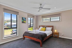 Ein Schlafzimmer mit einem Bett, einem Deckenventilator, großen Fenstern und Blick ins Freie.