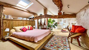 Un dormitorio rústico con cama tipo altillo, cabecera de madera, tragaluz y pequeño escritorio.