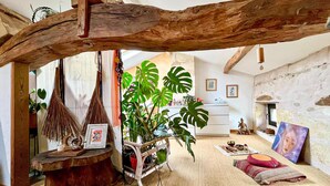 Una habitación rústica con vigas de madera a la vista, una planta grande, un banco de madera y un rincón de estar acogedor con cojines.