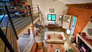 Amplio salón tipo loft con techo alto, una escalera, un sofá grande, una mesa de centro y un televisor.