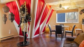 Una habitación con zona de comedor, una estatua, cortinas rojas y una ventana con vistas.
