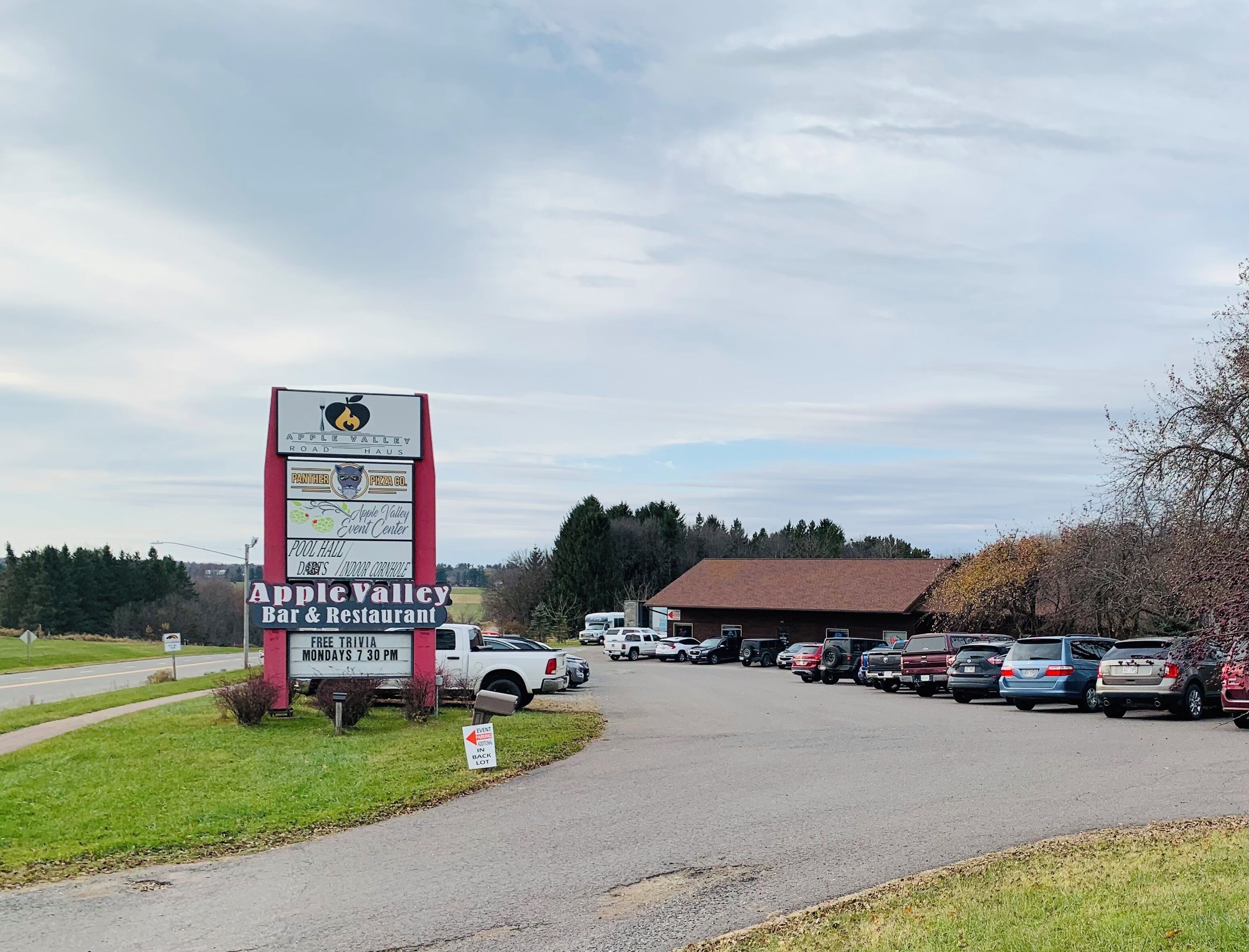 Een parkeerplaats met een groot bord voor Apple Valley Bar & Restaurant, inclusief een trivia-evenement.