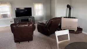 Una sala de estar con un televisor de pantalla plana, sillones de cuero, una silla blanca y un calentador blanco.