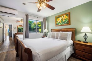 A bedroom with a large bed, a ceiling fan, a nightstand with a lamp, a painting on the wall, and a window with curtains. - Napili Point | Oceanfront 3 BR, Sleeps 12 | Car Incl. w/ 6+ Nights | NAP ML-2576 by KBM (Lahaina)
