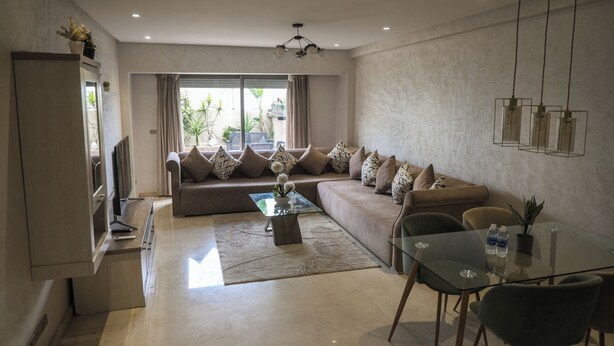 A modern living room with a sofa, a glass coffee table, a TV, and a dining area with chairs. - 2CH/2SDB - Modern & Bright - Wi-Fi - Garage - Streetcar 2 min (Casablanca)