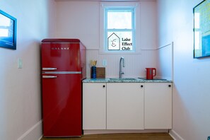 A compact kitchen with a red Galanz refrigerator, a small window, a sink, and a sign for the Lake Effect Club.