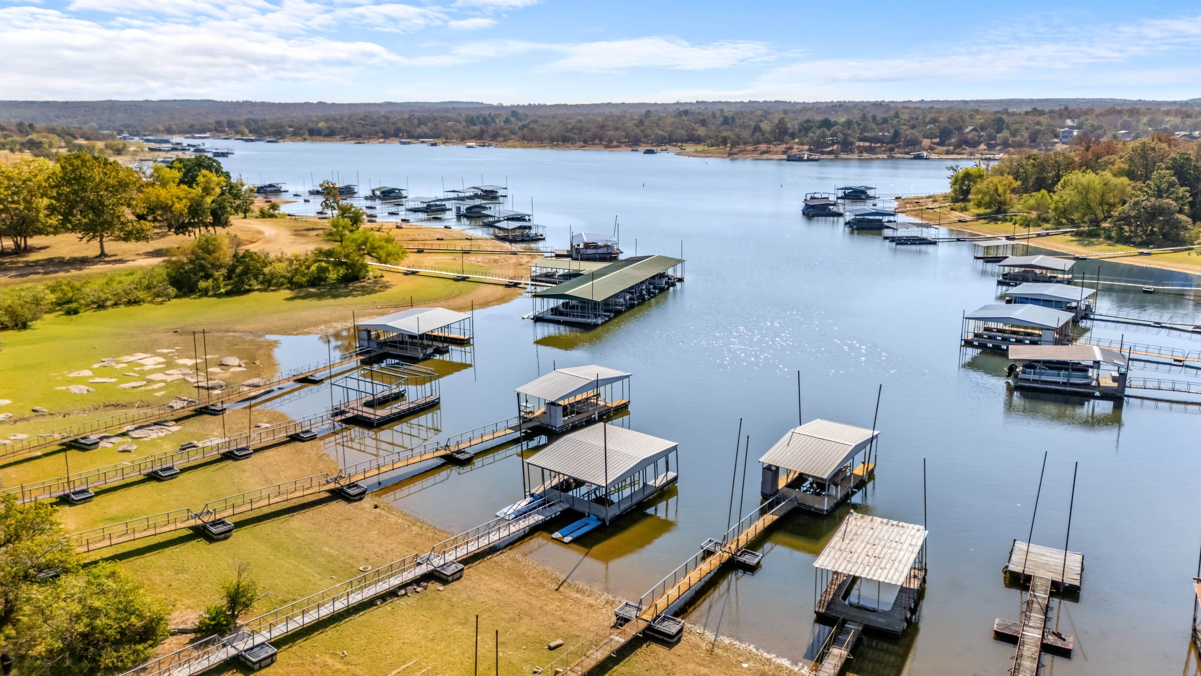 A marina with multiple docks and boats, surrounded by greenery and a distant tree line.
