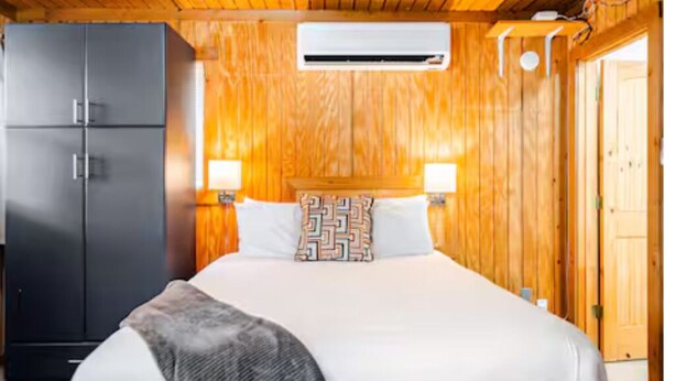 A wooden-paneled room with a bed, a wardrobe, and an air conditioning unit. - Bixby Cove Cabin #3 (Porum)