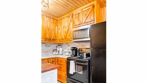 A kitchen with wooden cabinets, a black refrigerator, a stove, and a microwave. - Bixby Cove Cabin #3 (Porum)