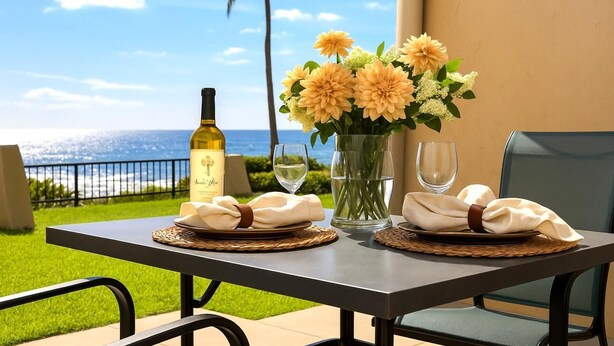 Une table dressée avec une bouteille de vin, des verres et un vase de fleurs, sur un balcon donnant sur l’océan.