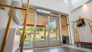 A hotel entrance with a sliding glass door, a metal cart, and a view of the outdoors.