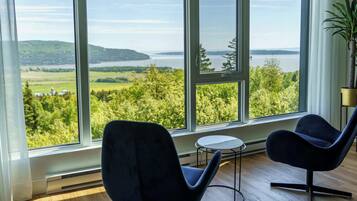 A room with large windows offering a view of a lake and greenery. There are two modern chairs and a small table.