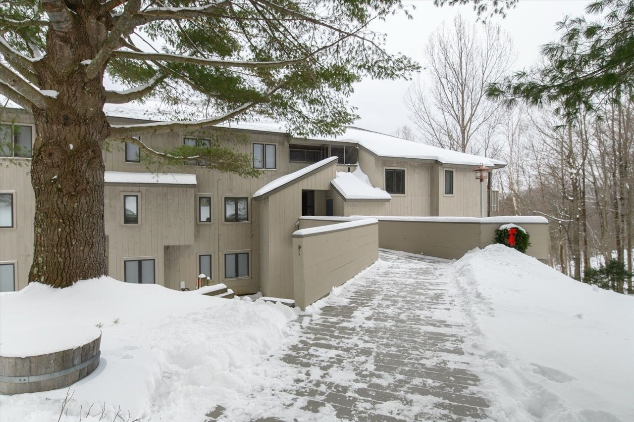 Un edificio de varios pisos con tejado nevado y un sendero que conduce a la entrada.