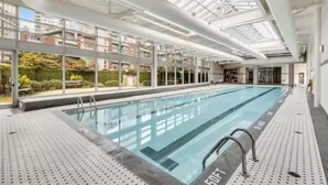 Una piscina interior con paredes de vidrio transparente, un deck con baldosas y un diseño arquitectónico moderno.