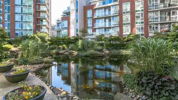 Zona residencial con edificios de apartamentos modernos, un pequeño estanque y jardines ajardinados.