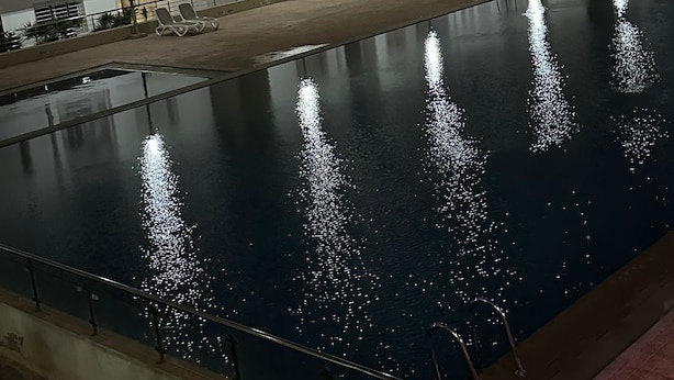 A swimming pool with reflections, surrounded by a building with multiple floors and windows. - Apartment agadirparking wifi swimming pool (Agadir)