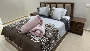 A neatly made bed with a patterned bedspread and pillows, a wooden headboard, and a nightstand with a drawer. - Apartment agadirparking wifi swimming pool (Agadir)