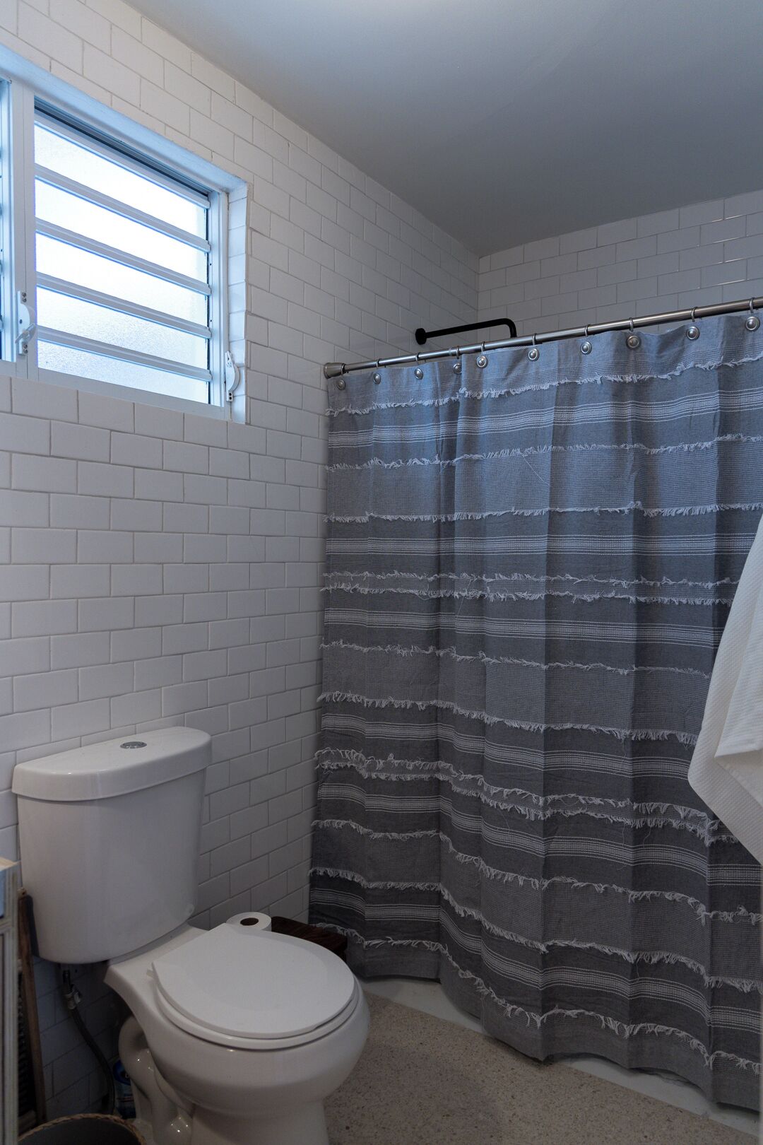 Un baño con inodoro blanco, una ventana con persianas y una cortina de ducha.