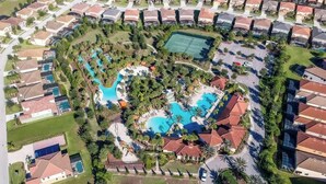 Vista aérea de una zona residencial con una piscina grande, canchas de tenis y céspedes bien cuidados.