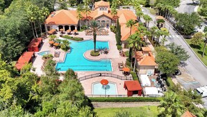 Eine Vogelperspektive zeigt ein Resort mit einem großen Schwimmbecken, mehreren Liegebereichen und einem gepflegten Garten.